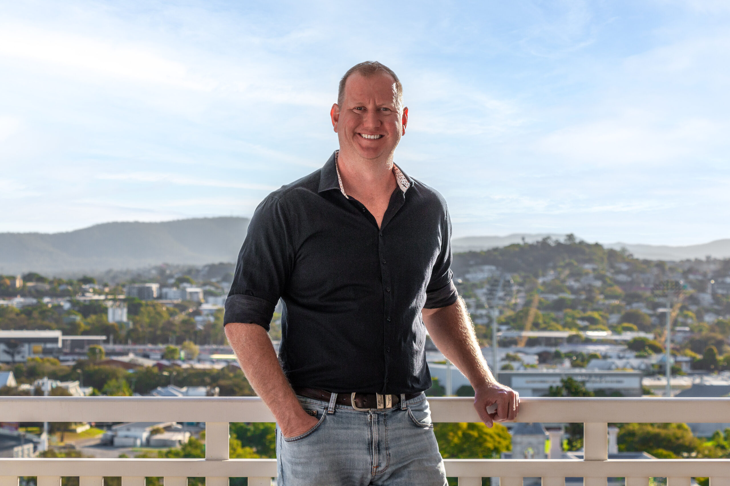 A man in a black shirt and blue jeans, smiling for the camera