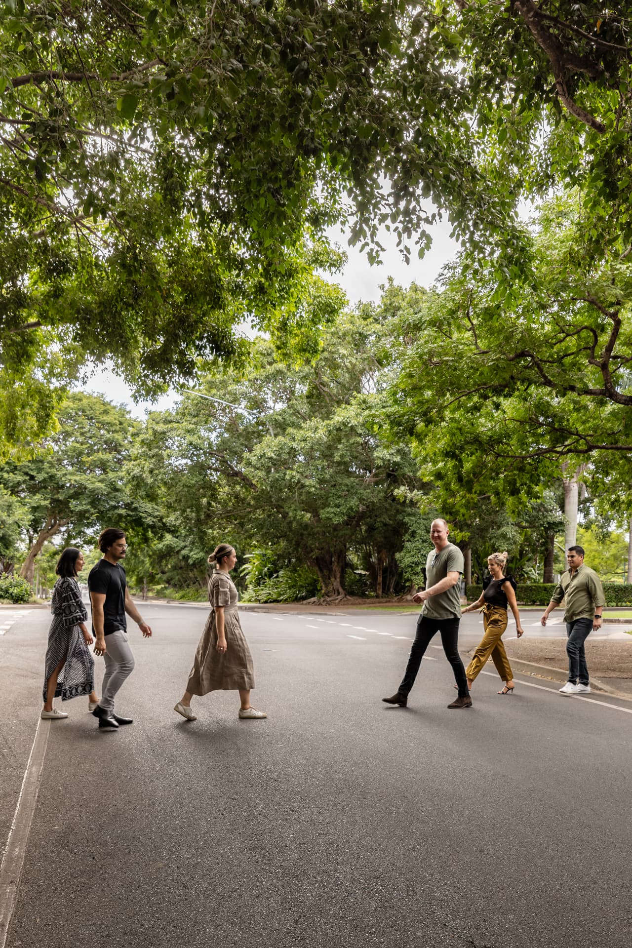 Group of people walking across a road with lots of trees either side.