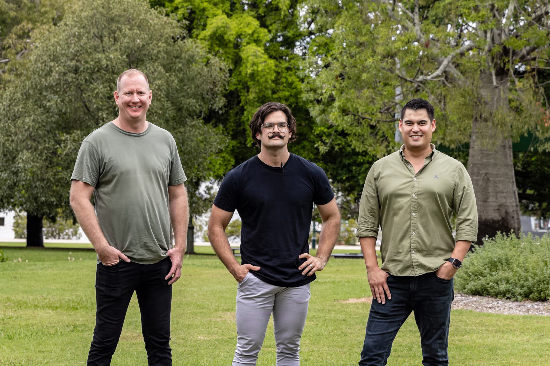 Three men standing in a park posting for the camera.